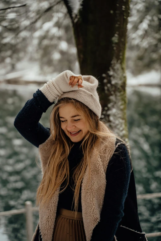 a woman standing next to a tree in the snow, trending on pexels, happening, head bent back in laughter, beanie, avatar image, fingerless gloves