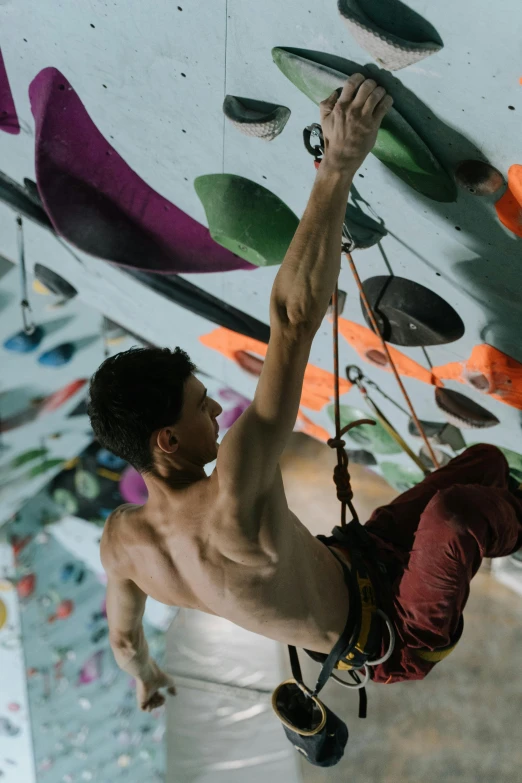 a man climbing up the side of a rock wall, things hanging from ceiling, maxwell boas, confident looking, ross tan