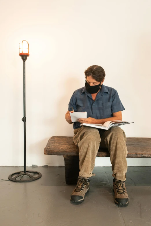 a man sitting on a bench reading a book, by Gavin Hamilton, arte povera, carbide lamp, covid, 7 feet tall, andrew bernstein