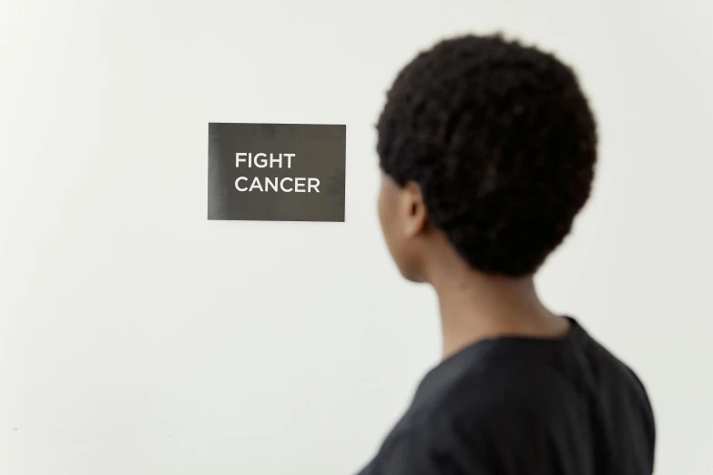 a man standing in front of a sign that says fight cancer, by Nina Hamnett, visual art, black, ignant, right angled view, women fighting men