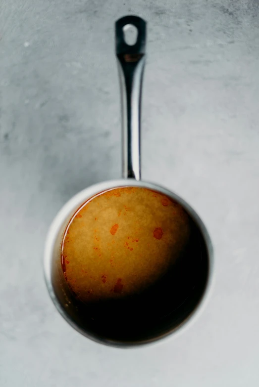 a cup of coffee sitting on top of a counter, holding hot sauce, on a gray background, zoomed out to show entire image, steel