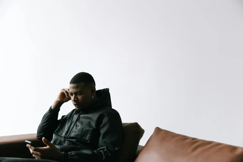 a man sitting on a couch talking on a cell phone, trending on pexels, visual art, wearing a black hoodie, man is with black skin, overcast mood, wearing a tracksuit