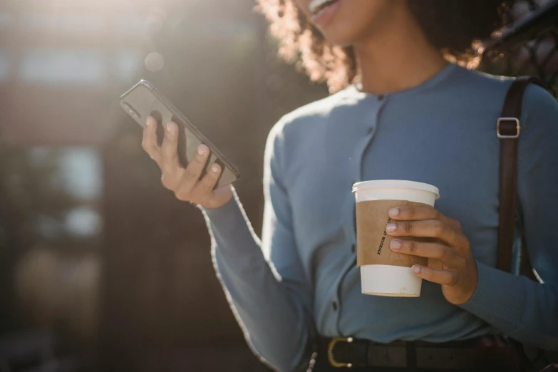 a woman holding a cup of coffee and a cell phone, trending on pexels, avatar image, sunlit, low-angle shot, light skin
