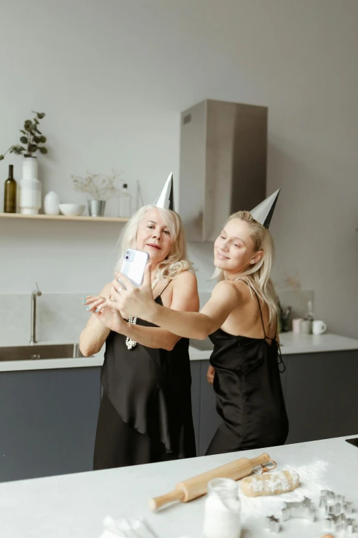 a couple of women standing next to each other in a kitchen, a polaroid photo, pexels contest winner, modernism, party hats, blonde and silver hair, bat ears, goddess checking her phone