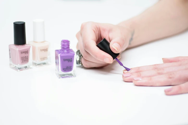 a close up of a person holding a bottle of nail polish, inspired by Eden Box, purple. ambient lightning, detail shot, lepra, set against a white background