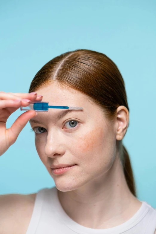 a woman combing her hair in front of a blue background, trending on pexels, renaissance, holding syringe, groomed eyebrows, detailed product image, square facial structure