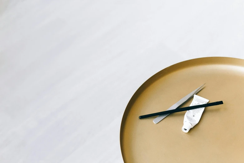 a close up of a clock on a table, inspired by David Chipperfield, trending on pexels, minimalism, gradient white to gold, holding a knife, metal lid, high angle