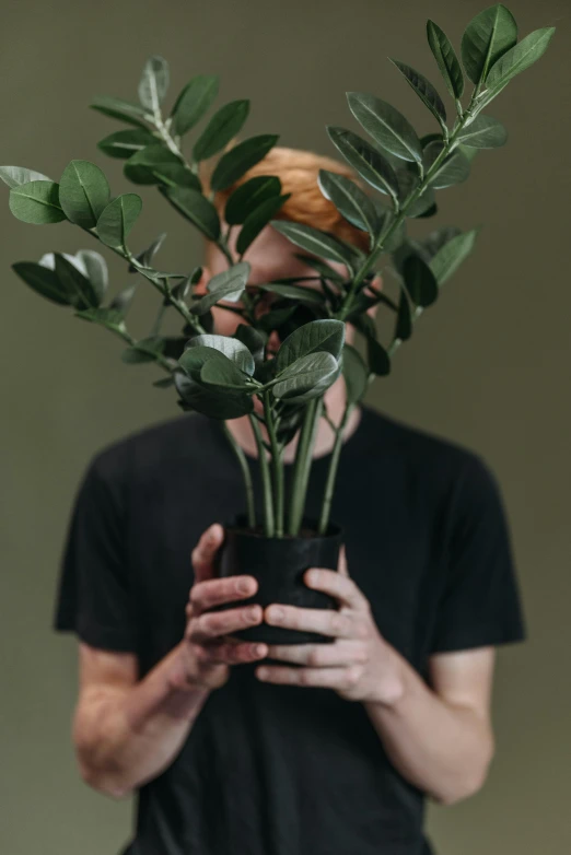 a man holding a potted plant in front of his face, inspired by Elsa Bleda, trending on unsplash, he is wearing a black t-shirt, muted green, ignant, humanoid flora