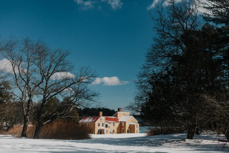 a house sitting in the middle of a snow covered field, by Jessie Algie, pexels contest winner, colonial style, wes anderson background, lakeside, sunny day time