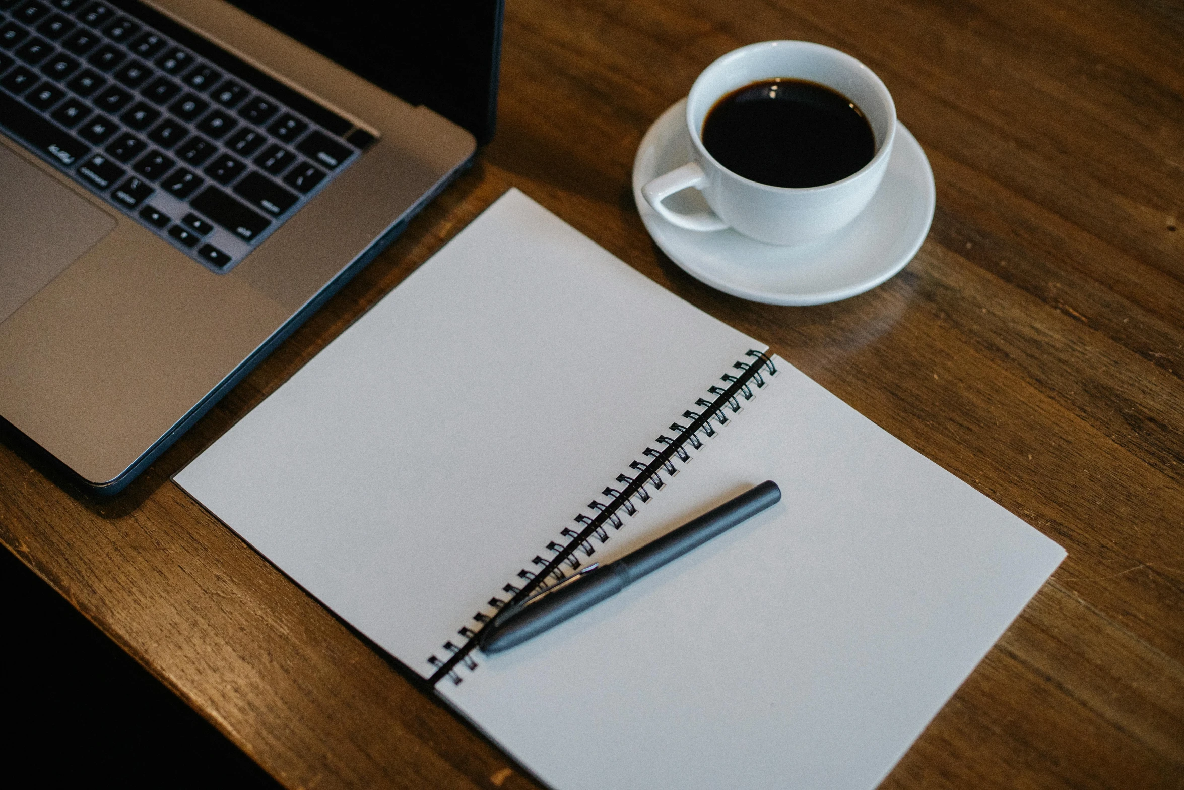 a laptop computer sitting on top of a wooden desk next to a cup of coffee, a drawing, pexels contest winner, black ball pen on white paper, background image, 9 9 designs, notebook