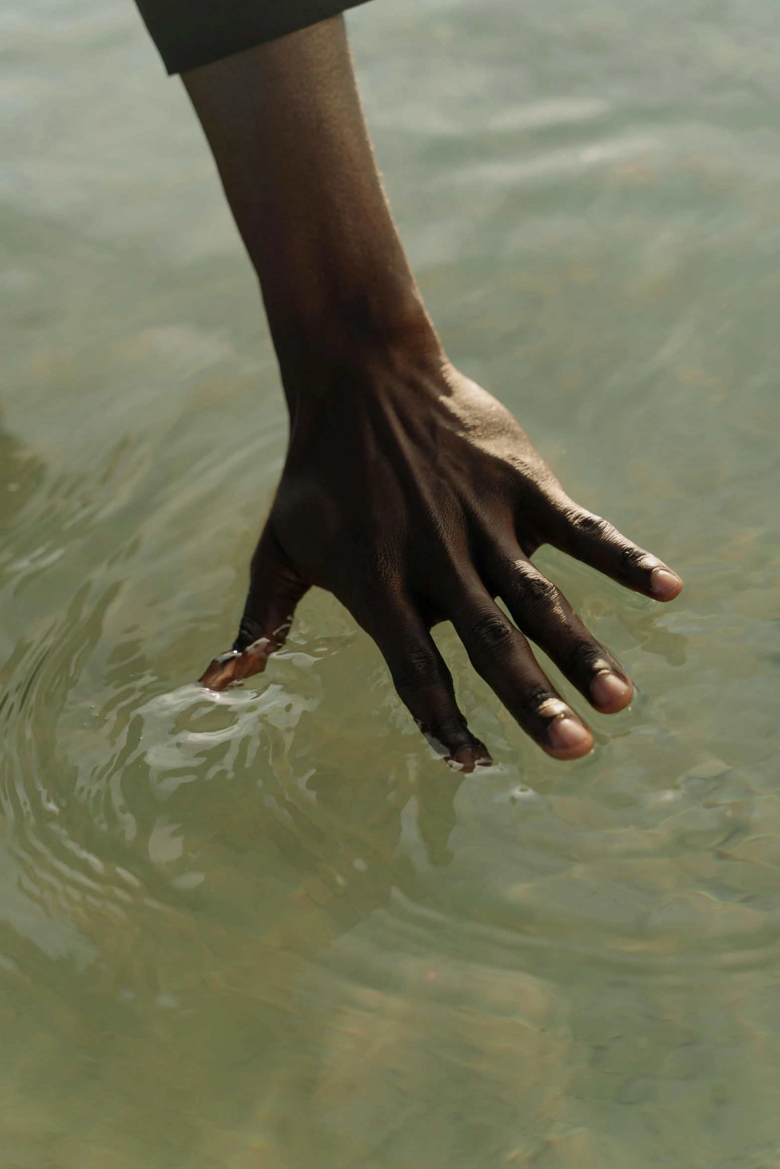 a person reaching for a frisbee in the water, by Arabella Rankin, hurufiyya, man is with black skin, close-up of thin soft hand, ignant, in an african river