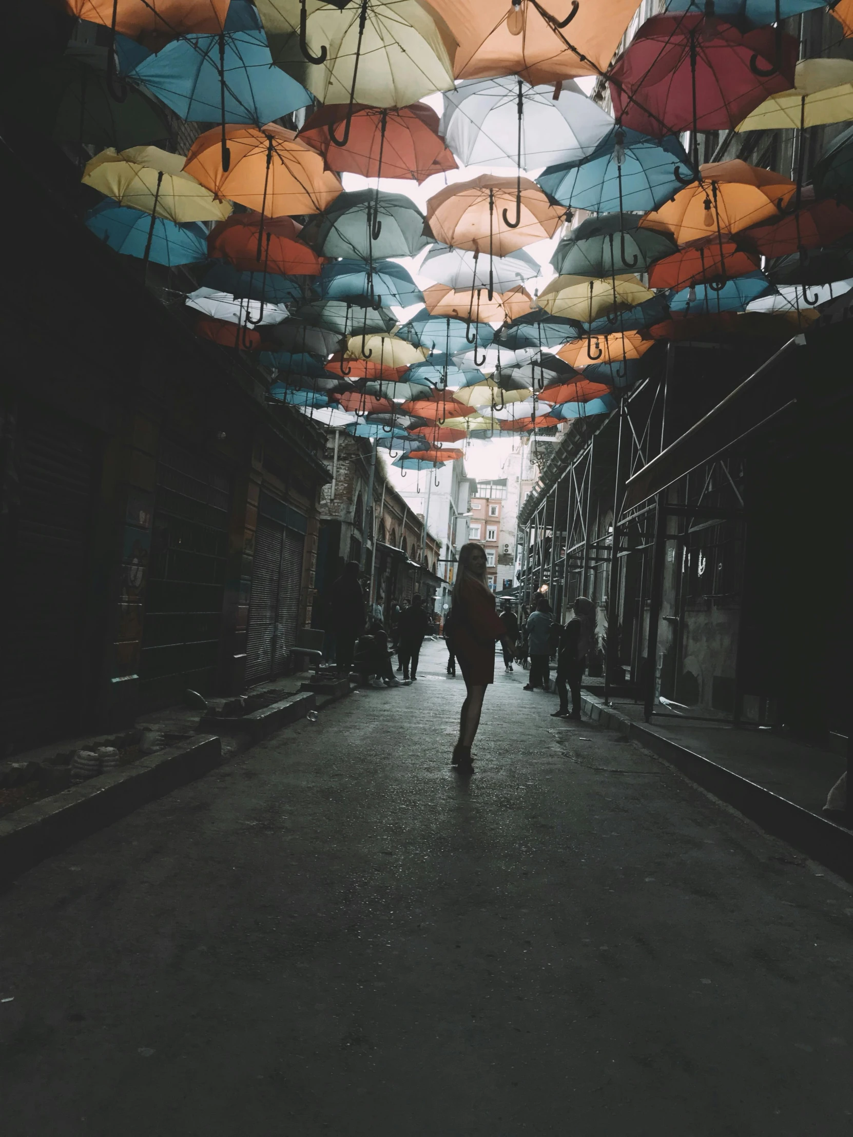 a person walking down a street with umbrellas overhead, a colorized photo, unsplash contest winner, street art, girl under lantern, trending on vsco, alternate album cover, abandoned vibes