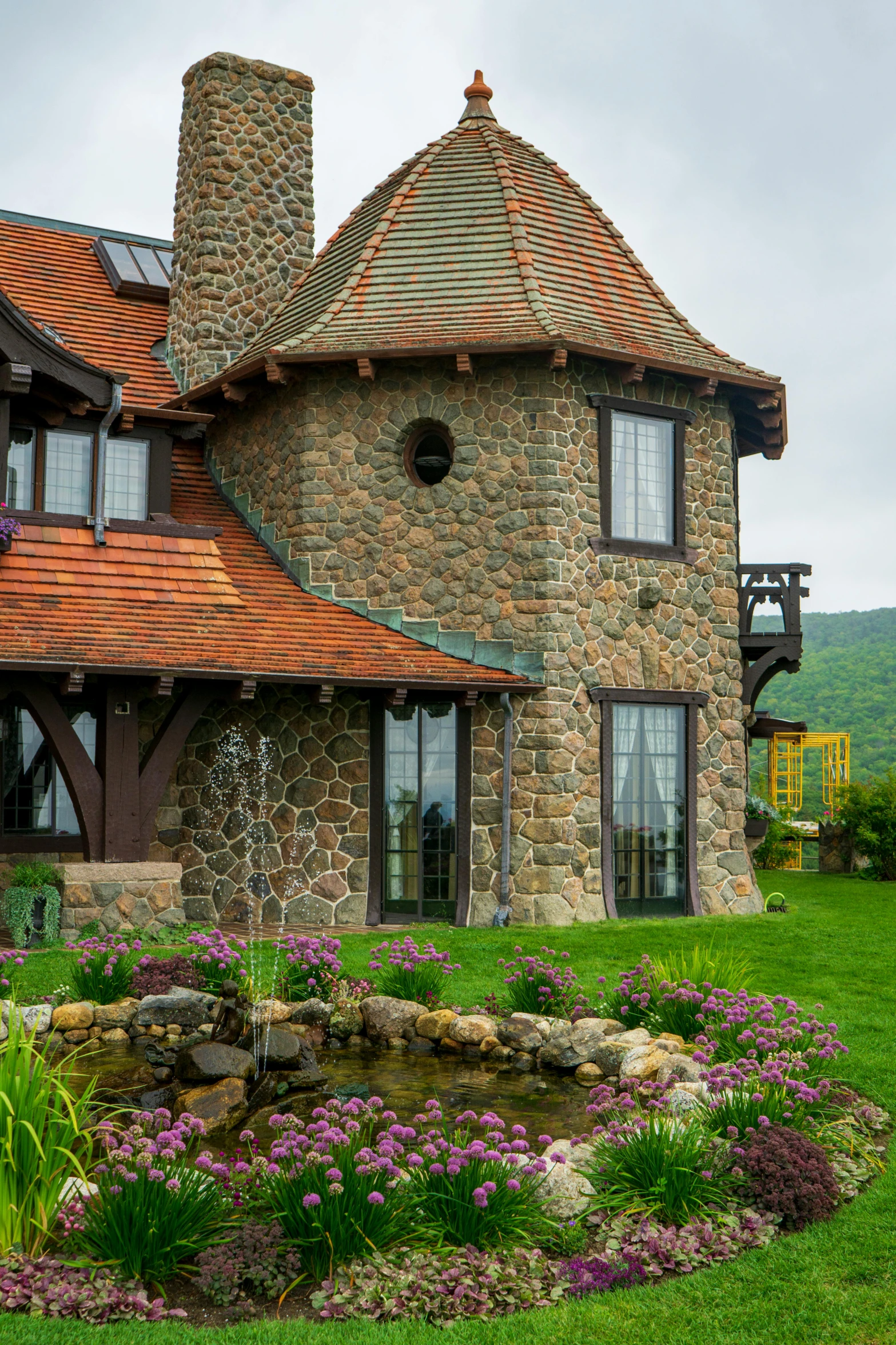 a stone house sitting on top of a lush green field, inspired by Edward Willis Redfield, arts and crafts movement, turrets, lake view, cottagecore, resort