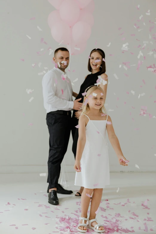 a woman in a white dress standing next to a man and a little girl, falling petals, in a photo studio, promotional image, third trimester