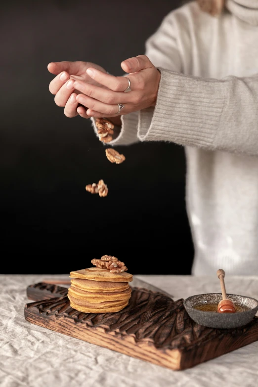 a woman is sprinkling nuts on a stack of pancakes, a still life, inspired by Jan Müller, trending on pexels, portrait image, natural wood top, product introduction photo, plating