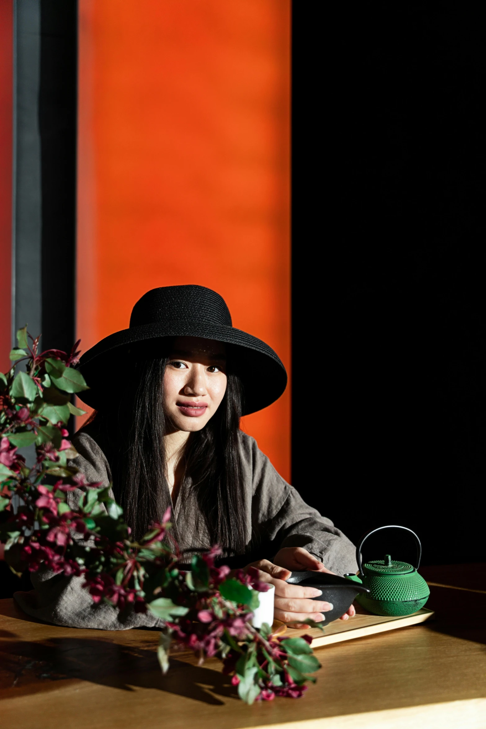 a woman in a black hat sitting at a table, inspired by Li Di, unsplash, visual art, ikebana, tilt and orange, asian descent, full colour