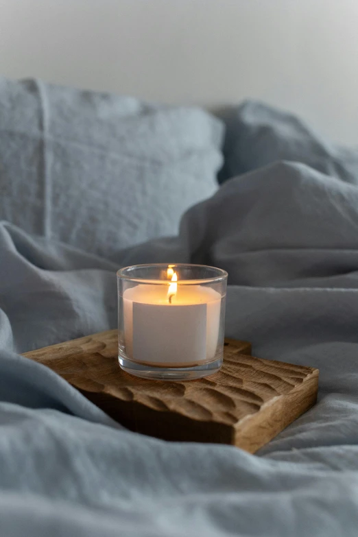 a candle sitting on top of a wooden tray on a bed, by Helen Stevenson, soft grey and blue natural light, small, slate, quiet