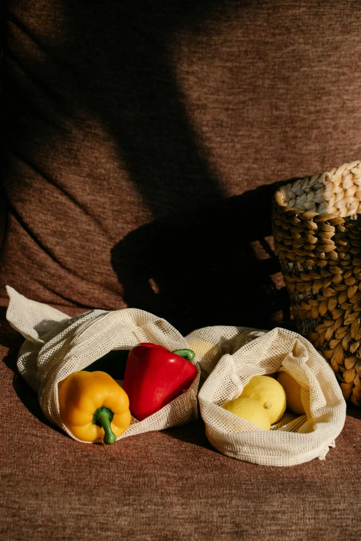 a basket filled with vegetables sitting on top of a couch, a still life, unsplash, holding mesh bag with bagels, yellow and red, sustainable materials, ecru cloth