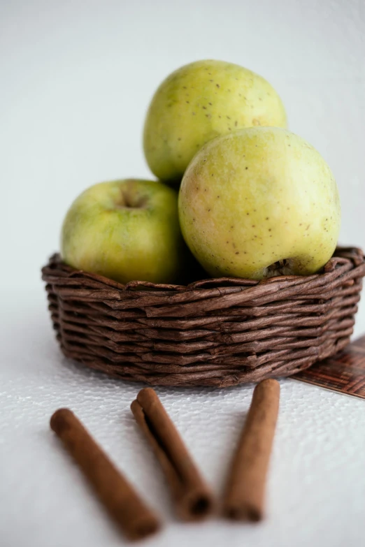 a basket filled with green apples next to cinnamon sticks, 4l, petite, battered, hispanic