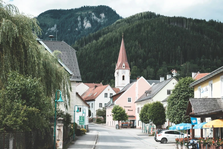 a town street with a church steeple in the background, by Sebastian Spreng, pexels contest winner, mountainous setting, square, a green, laid - back