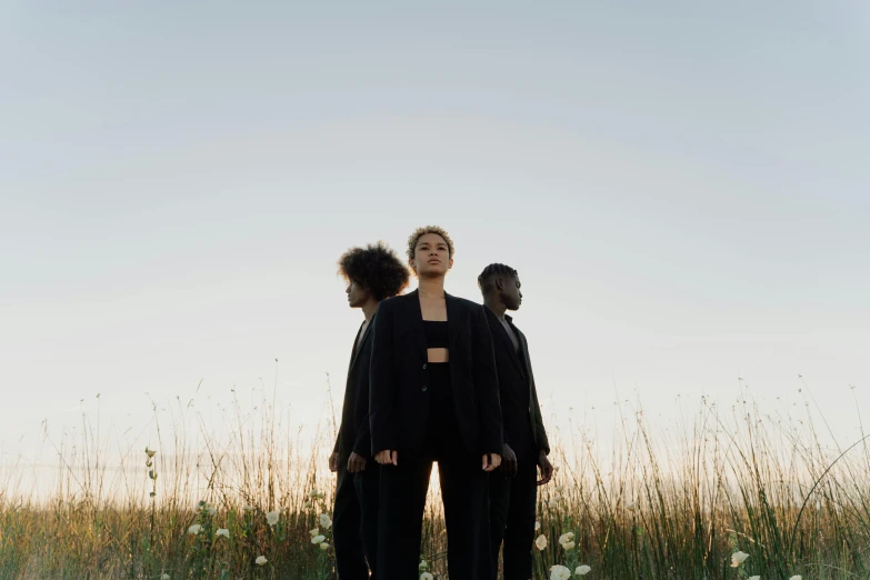 two people standing in a field of tall grass, an album cover, by Emma Andijewska, pexels contest winner, antipodeans, three women, wearing causal black suits, ashteroth, full-body view
