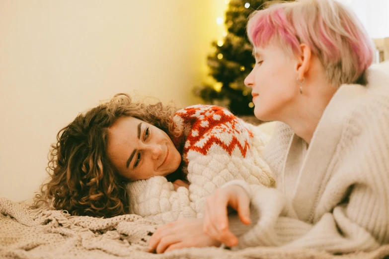 a couple of women laying on top of a bed, trending on pexels, wearing festive clothing, looking at each other mindlessly, pale - skinned, looking from shoulder