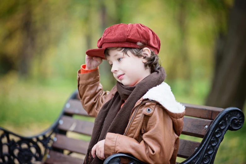 a young boy sitting on top of a wooden bench, inspired by Kate Greenaway, trending on pixabay, wearing a brown leather coat, wearing a french beret, picnic, warm color clothes