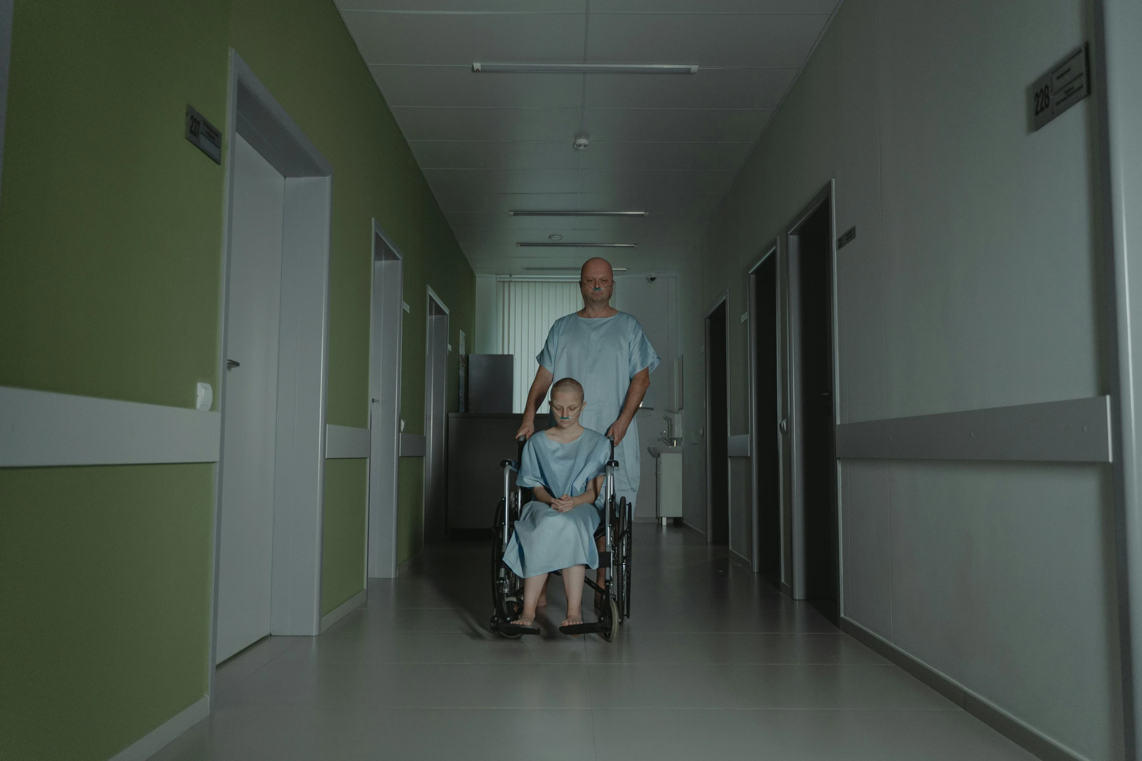 a man pushing a woman in a wheelchair down a hallway, an album cover, by Attila Meszlenyi, pexels, hyperrealism, candy hospital room, nighttime, high quality wallpaper, worksafe. cinematic