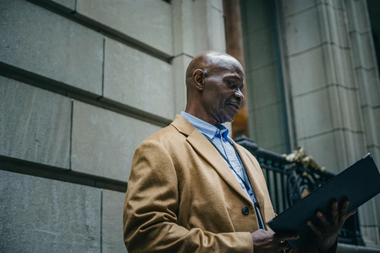 a man standing in front of a building holding a laptop, by Joseph Severn, pexels contest winner, augusta savage, holding court, old man, profile image