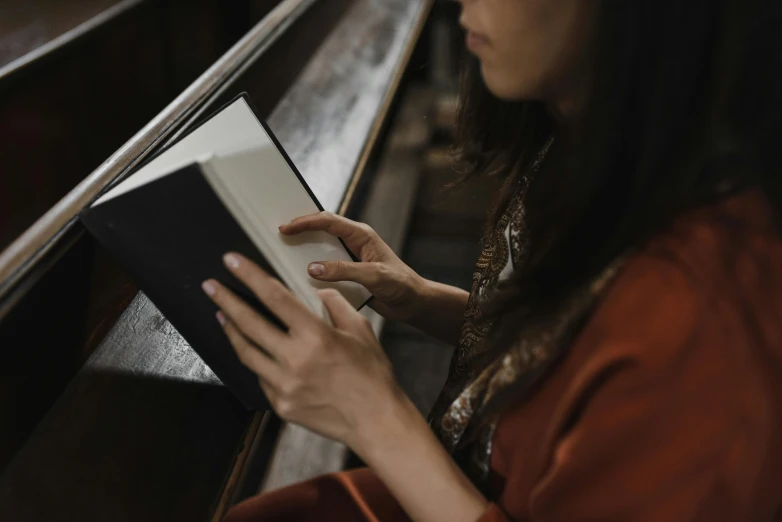 a woman sitting on a bench reading a book, by Joseph Severn, pexels contest winner, renaissance, in a church. arstation, an asian woman, sleek hands, thumbnail