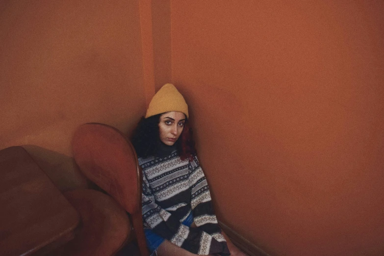 a woman sitting on a chair in a room, inspired by Elsa Bleda, trending on pexels, antipodeans, wearing beanie, aida muluneh, orange skin, wearing sweater
