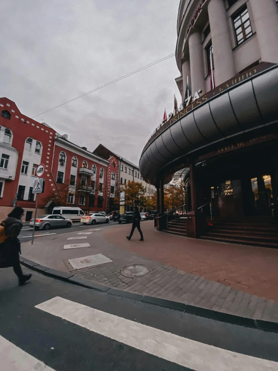 a man riding a skateboard down a street next to tall buildings, by Emma Andijewska, pexels contest winner, art nouveau, russian cinema, red building, during autumn, wide angle establishing shot