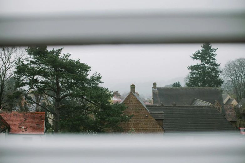 a view of a city through a window, a picture, unsplash, roofed forest, 5 0 mm kodak, small town, grey sky