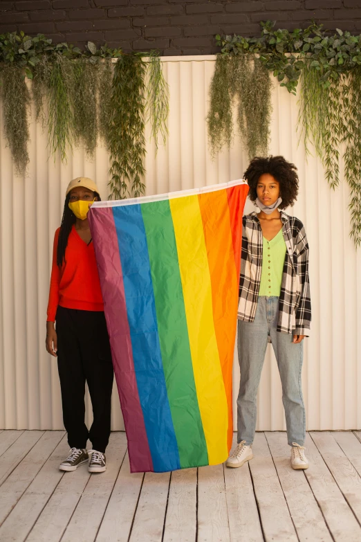 two women standing next to each other holding a rainbow flag, a picture, trending on pexels, diverse, indoor picture, two male, cardboard