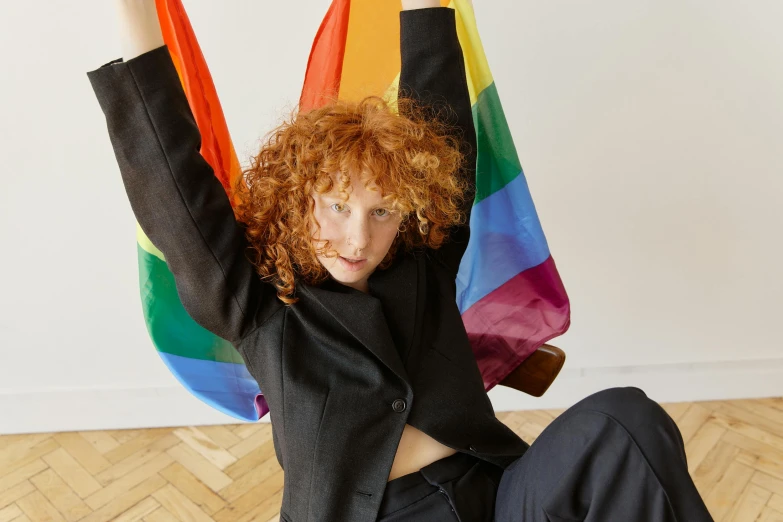 a woman sitting on the floor holding a rainbow flag, by Nina Hamnett, renaissance, with curly red hair, soft vinyl, flag in hands up, girl in suit