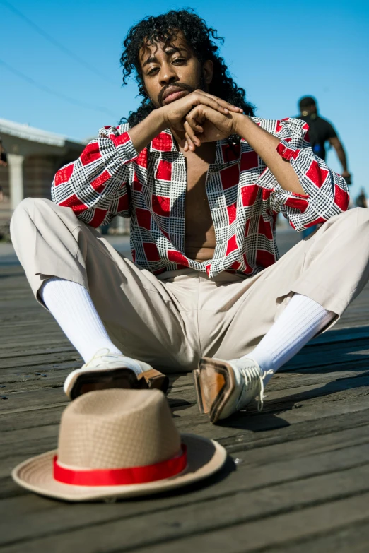 a man sitting on top of a wooden floor next to a hat, by Nina Hamnett, trending on pexels, renaissance, wearing a colorful men's suit, ashteroth, boardwalk, wearing off - white style