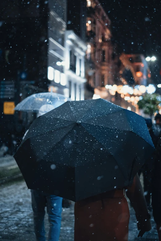 a group of people walking down a street holding umbrellas, snowfall at night, unsplash photography, close - up photo, ☁🌪🌙👩🏾