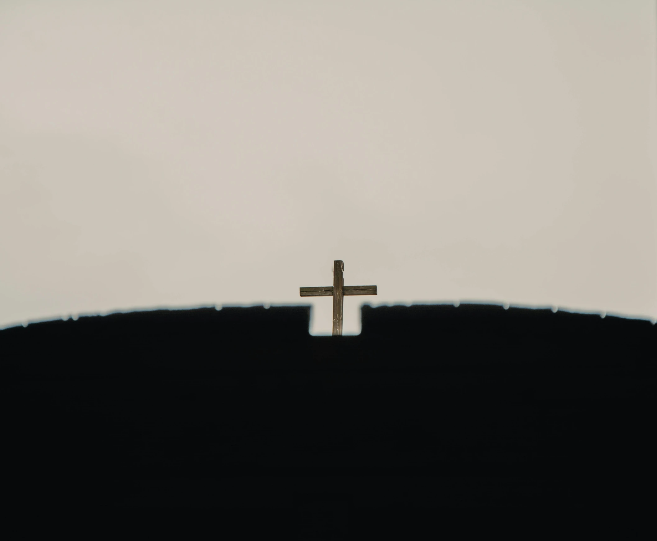 a cross on top of a hill on a cloudy day, by Attila Meszlenyi, unsplash, minimalism, shadow, black jesus, journalism photo, religión