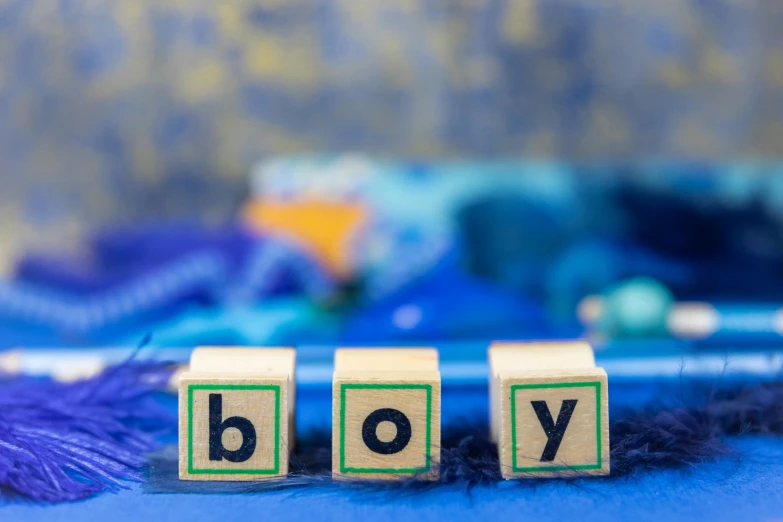 wooden blocks spelling the word boy on a blue background, by Georgina Hunt, pixabay, graffiti, pregnant, body shot, thumbnail, cubes on table