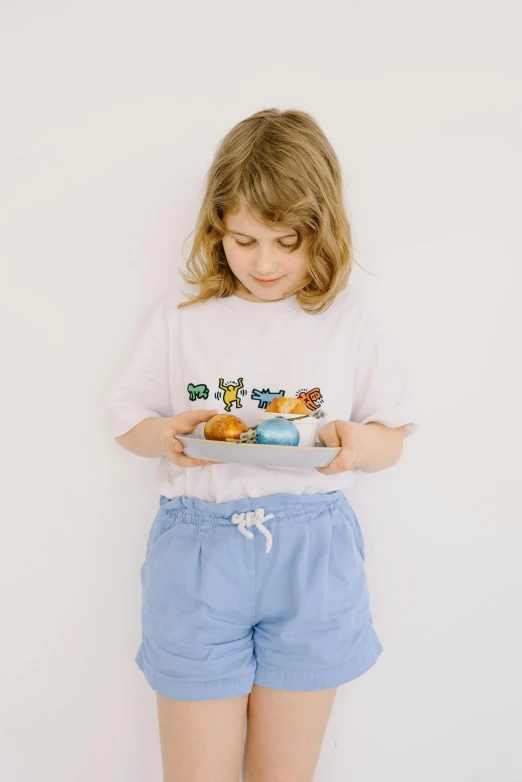 a little girl holding a plate of donuts, inspired by Elsa Beskow, pexels contest winner, visual art, white t-shirt, butterfly embroidery, high resolution product photo, wearing pants and a t-shirt