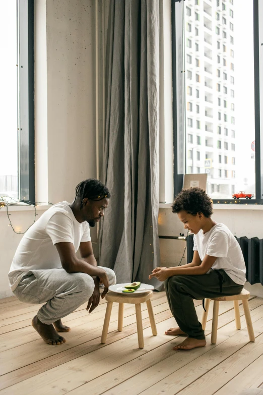 a man and a boy sitting on stools in front of a window, snacks, black man, dad energy, apartment