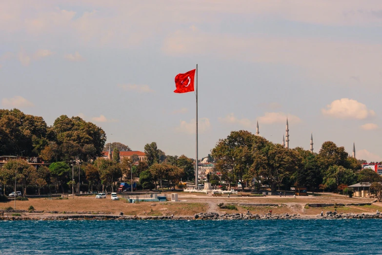 a red flag flying over a body of water, a colorized photo, pexels contest winner, hurufiyya, turkey, 🚿🗝📝, viewed from the ocean, parks and monuments