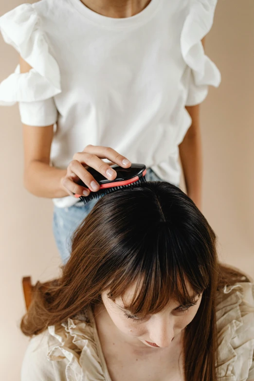 a woman is combing another woman's hair, by Nicolette Macnamara, trending on pexels, plain background, detailed product image, coral brown hair, covered in