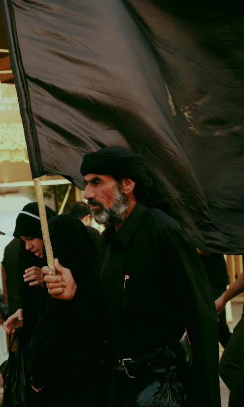 a group of men standing next to each other holding a flag, pexels, hurufiyya, wearing black clothes, ( ( theatrical ) ), with his long black hair, walk in a funeral procession