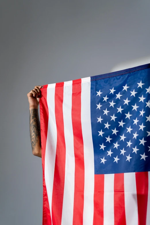 a man holding an american flag against a gray background, an album cover, trending on unsplash, wiz khalifa, ultrawide image, multiple stories, close up front view