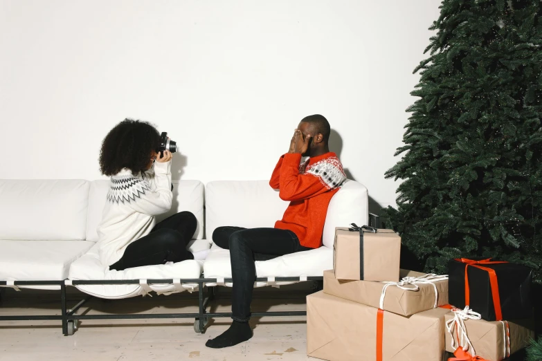 a couple of women sitting on a couch next to a christmas tree, a photo, pexels contest winner, visual art, black man, behind the scenes photo, virgil abloh, taking a picture