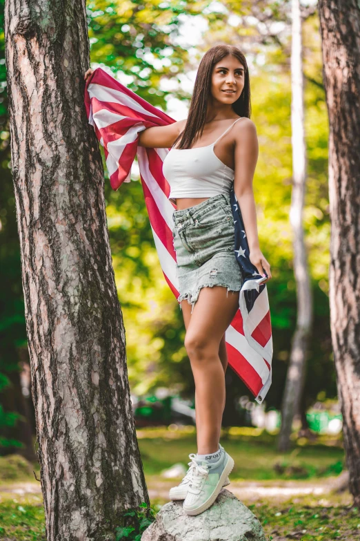 a woman standing on a rock holding an american flag, a portrait, pexels contest winner, on trees, :: madison beer, anna nikonova aka newmilky, legs