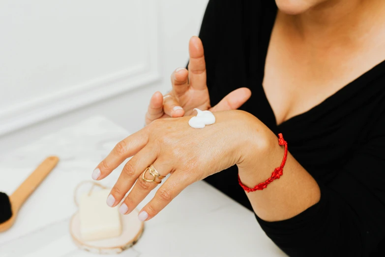 a woman sitting at a table with a lot of cream on her hand, trending on pexels, red jewelry, silicone skin, manuka, professional product shot