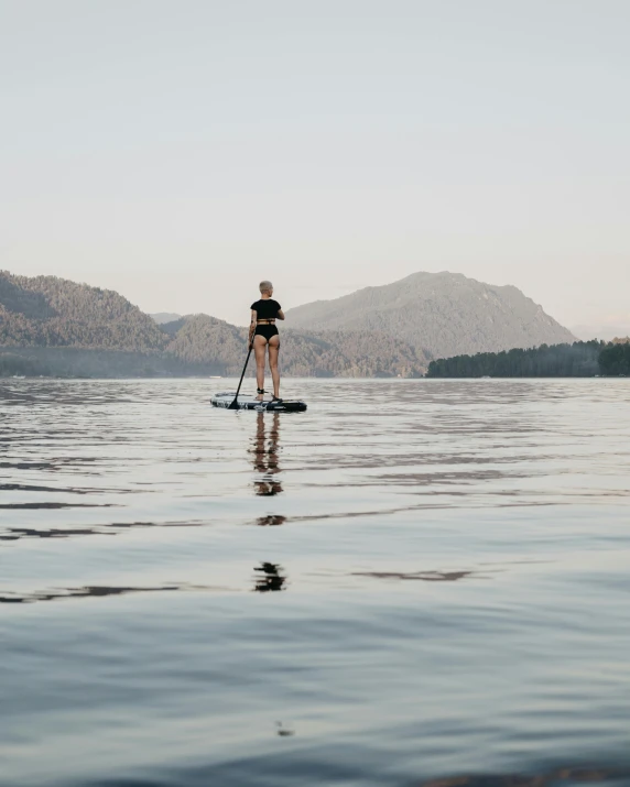 a man riding a paddle board on top of a lake, by Jessie Algie, an epic non - binary model, haida gwaii, trending photo, thumbnail