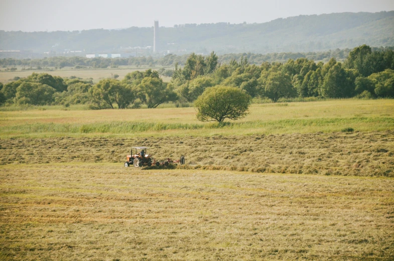 a tractor that is sitting in the grass, by Attila Meszlenyi, unsplash, land art, villagers busy farming, seen from a distance, stålenhag, sydney park